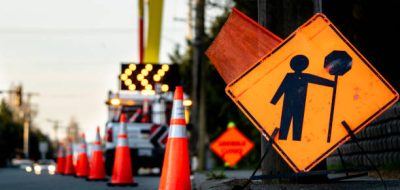 Lane closure on a busy road due to maintenance signs detour traffic temporary street work orange lighted arrow, barrels, and cones.